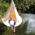 Child sitting in a hanging chair by a body of water with trees in the background