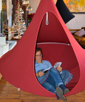 Person reading a book inside a red hanging pod in a modern living room.