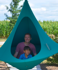 Two people inside a teal hanging pod with a cornfield in the background