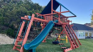 Wooden playset installed on a slope in Bulverde, TX with a monkey bar, slide, ladders, swings, and rock wall.