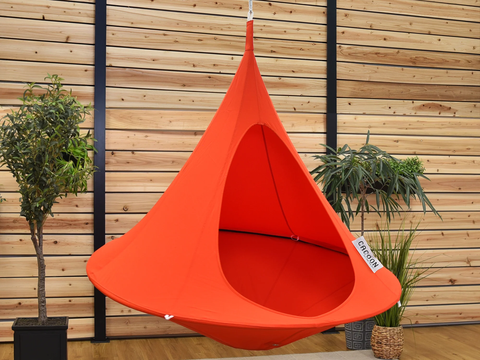 Orange hanging chair against a wooden wall with plants around