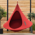 Red hanging pod chair against a wooden wall with plants.
