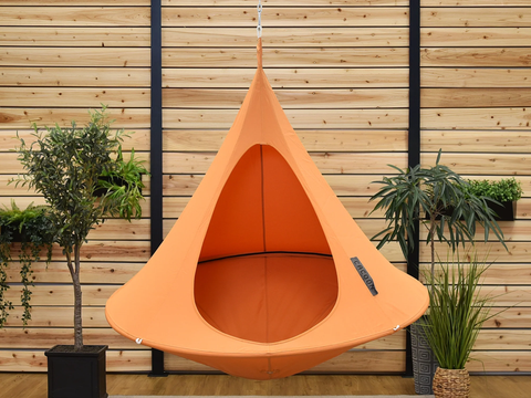 Orange hanging pod chair in a room with wooden walls and potted plants.