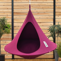 Purple hanging chair with a brand label against a wooden wall with plants.