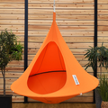 Orange hanging chair with a brand label against a wooden wall with plants.