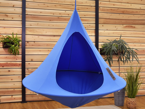 Blue hanging chair against a wooden wall with plants.