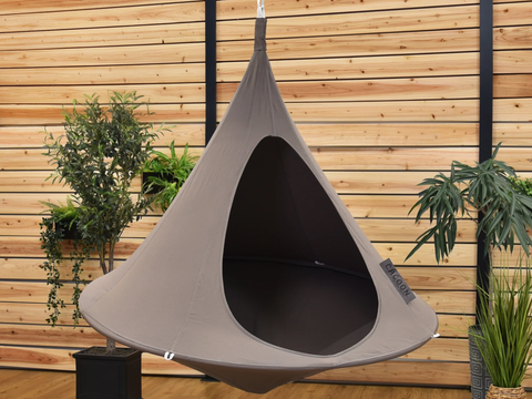 Gray hanging pod chair against a wooden wall with plants