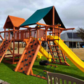 Children's playground with wooden structure, slides, and climbing elements on grass.
