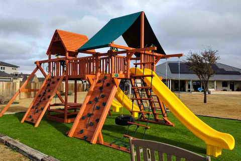 Children's playground with wooden structure, slides, and climbing elements on grass.