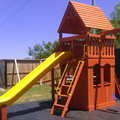 Wooden playground set with a yellow slide and red roof in an outdoor setting.