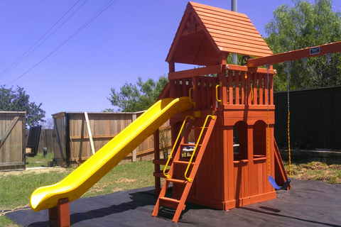 Wooden playground set with a yellow slide and red roof in an outdoor setting.