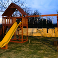 Wooden playground set with a yellow slide and monkey bars at dusk.