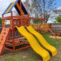 Children's playground with wooden structure, yellow slide, and climbing elements in a backyard setting.