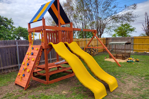 Children's playground with wooden structure, yellow slide, and climbing elements in a backyard setting.