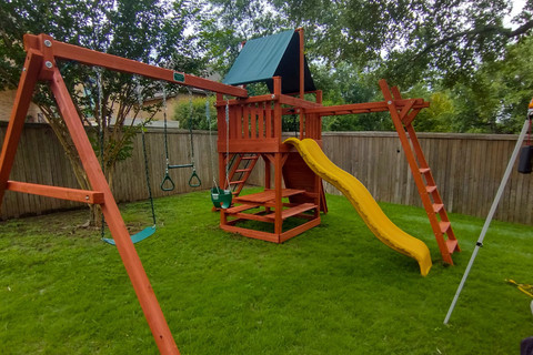 Wooden playground set with a yellow slide and green roof in a backyard.