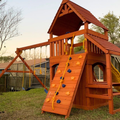 Wooden playset with climbing wall and slide in a backyard setting