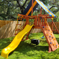 Children's playground set with yellow slide and climbing wall in a backyard.