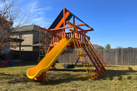 Playset with yellow slide and climbing structure in a backyard