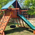 Wooden playground set with slides and swings in a backyard setting.