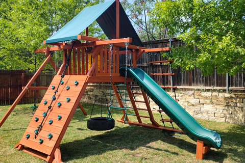 Wooden playground set with slides and swings in a backyard setting.