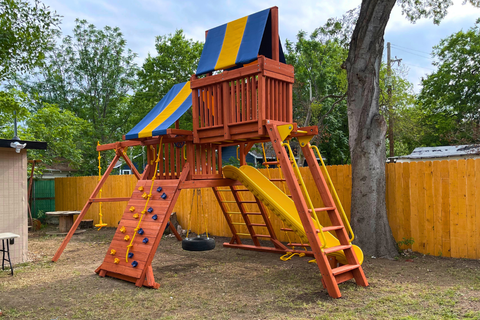 Colorful playground structure with slides and climbing elements in a backyard setting.