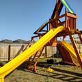 Wooden playground with yellow slide and blue climbing structure in a backyard.