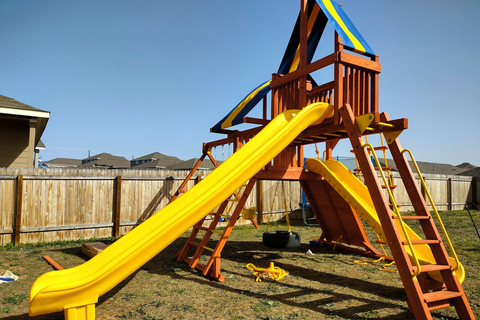 Wooden playground with yellow slide and blue climbing structure in a backyard.
