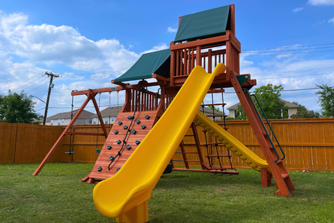 Children's playground with a yellow slide and climbing structure on a grassy area.