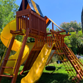 Children's playground with yellow slides and wooden structure in a park setting.