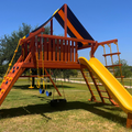 Colorful playground with a yellow slide and swings on a grassy area.