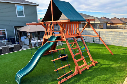 Children's playset with a green slide and red climbing structure on a grassy backyard.
