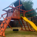 Wooden playground with a yellow slide and climbing wall in a backyard.