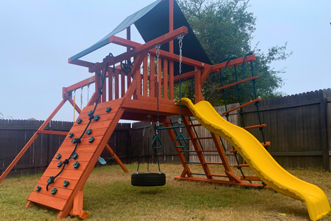 Wooden playground with a yellow slide and climbing wall in a backyard.