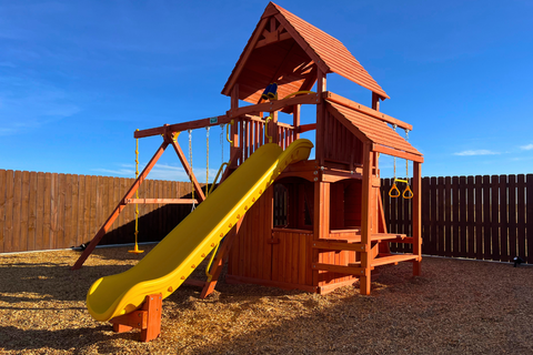 Wooden playground set with a yellow slide against a blue sky.