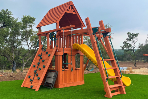 Wooden playground set with slides and climbing structures on a grassy area.