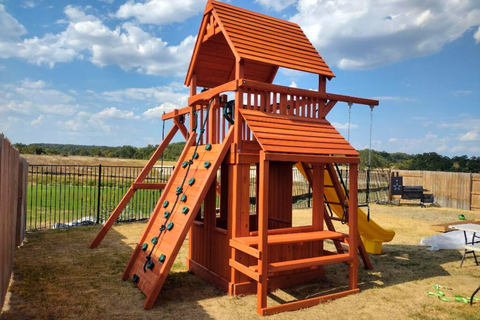 Wooden playset with slides and climbing wall in a backyard setting