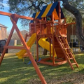 Children's playground with swings, slide, and climbing structure in a backyard setting.
