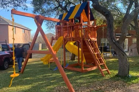 Children's playground with swings, slide, and climbing structure in a backyard setting.
