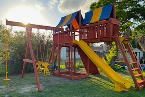 Children's playground with a red play structure, yellow slide, and swings in a park setting.