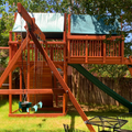 Wooden playground swing set with slides and swings in a backyard setting.