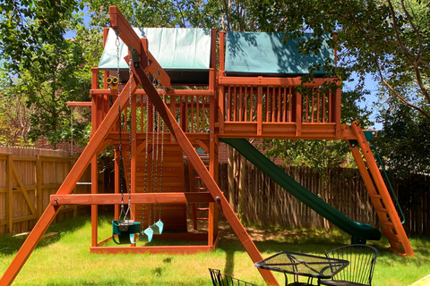 Wooden playground swing set with slides and swings in a backyard setting.