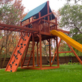 Wooden playground with slides and climbing structures in a park setting.