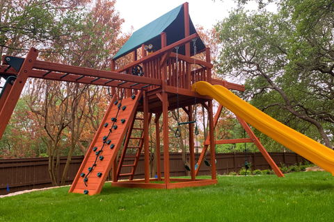 Wooden playground with slides and climbing structures in a park setting.