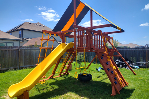 Children's playground with yellow slide, swings, and climbing structure on grass