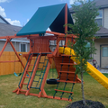 Children's playset with a green roof and yellow slide in a backyard.
