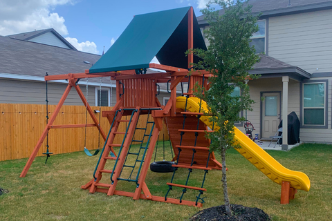 Children's playset with a green roof and yellow slide in a backyard.