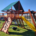 Wooden playground structure with a yellow slide and climbing wall on a grassy area.