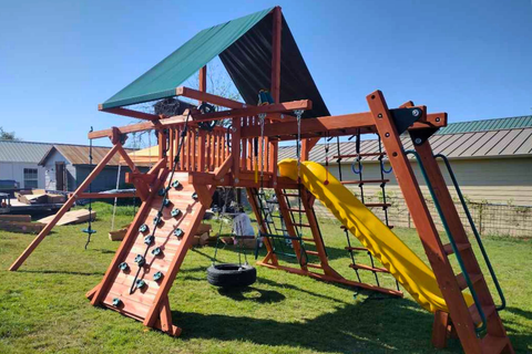 Wooden playground structure with a yellow slide and climbing wall on a grassy area.