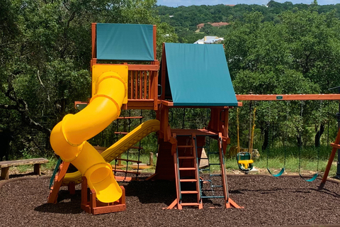Children's playground with a yellow slide and blue roofs in a park setting.