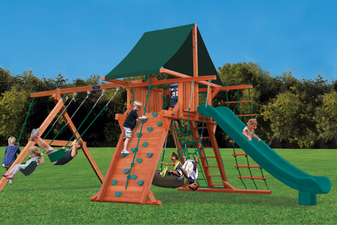 Children playing on a wooden playground set with green slide and climbing structure.